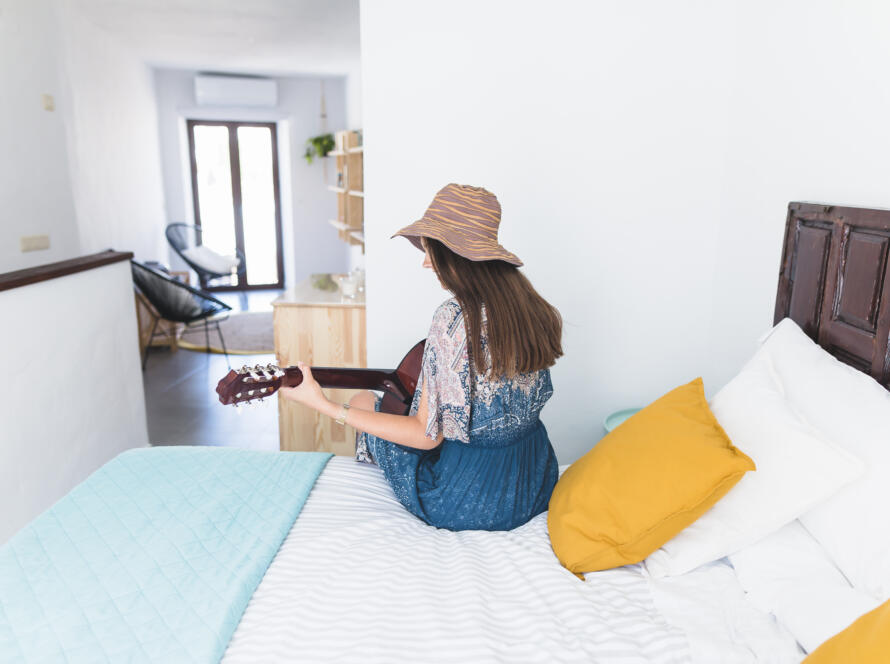 rear view woman sitting bed playing guitar » StayBooked